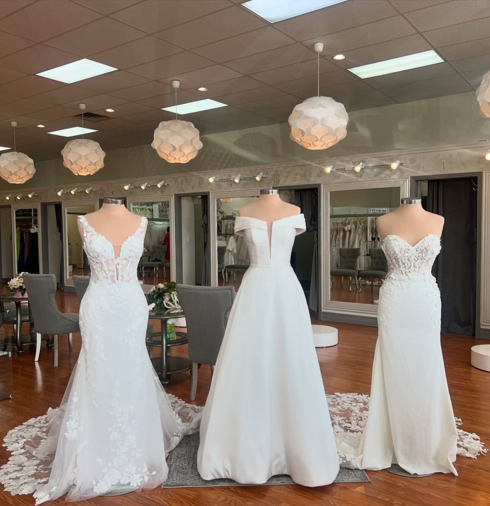 Three white wedding gowns on mannequins in bridal boutique showroom with geometric pendant lights