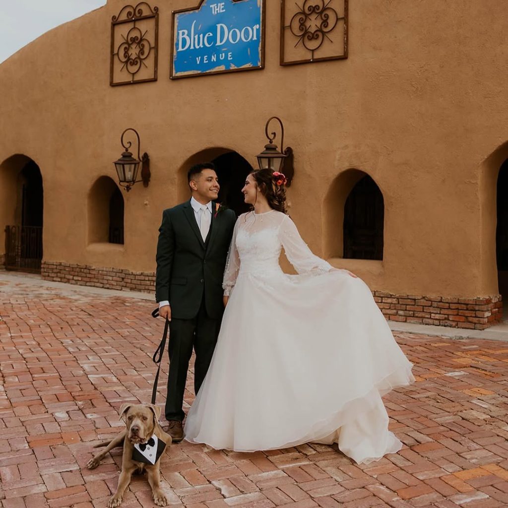 Bride and groom posing outside adobe-style building with distinctive blue door at Blue Door Venue