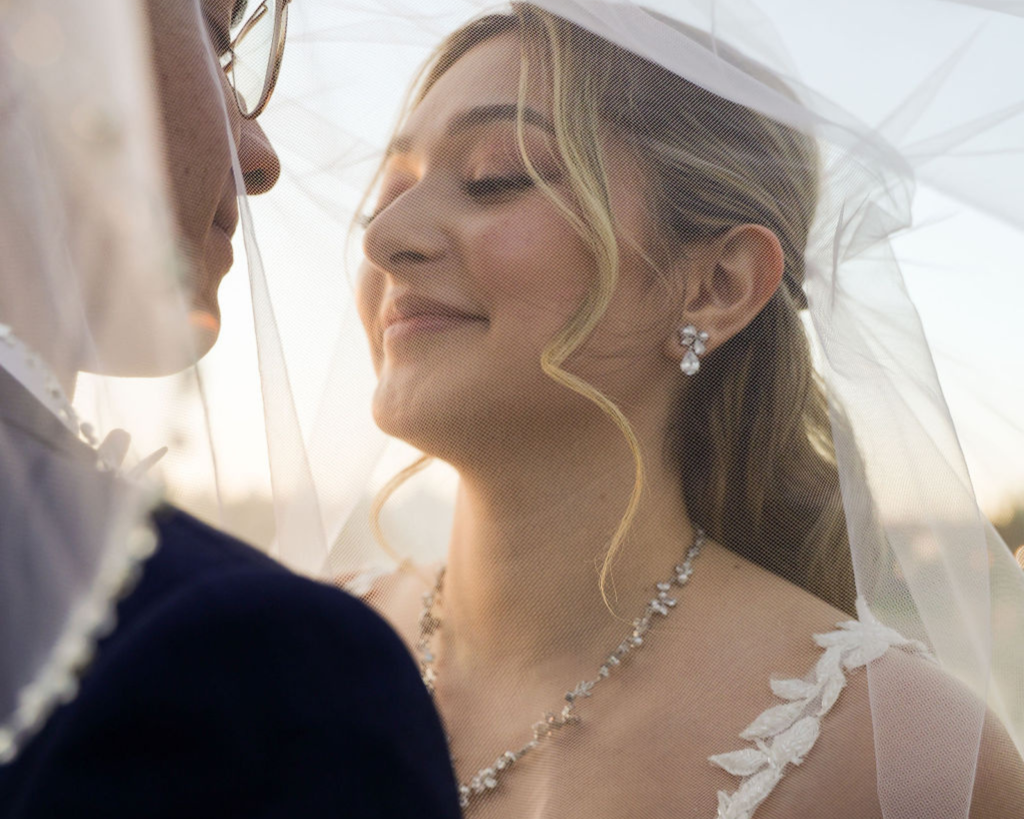 Wedding officiant conducting outdoor ceremony for couple holding hands under pergola decorated with white flowers and string lights