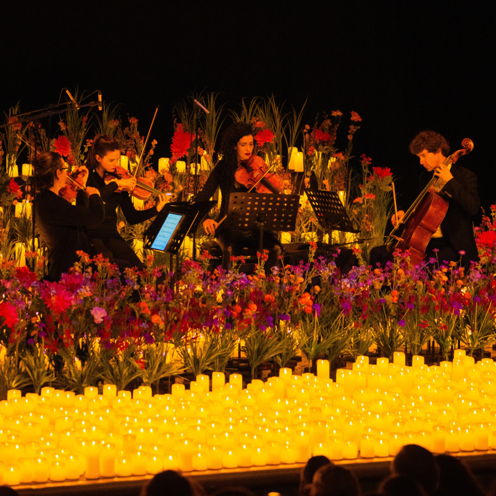 String quartet performing on stage surrounded by vibrant flowers and glowing candles at evening wedding ceremony