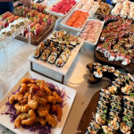 Elaborate sushi spread with tiered displays of colorful rolls, nigiri, and shrimp arranged on wooden platters