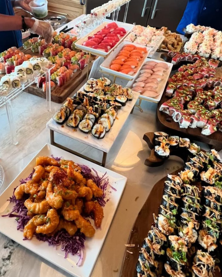 Elaborate sushi spread with tiered displays of colorful rolls, nigiri, and shrimp arranged on wooden platters
