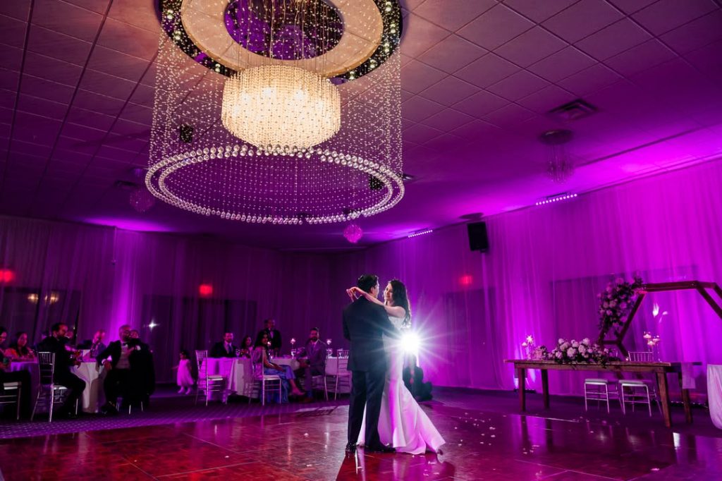 First dance under circular chandelier with dramatic purple uplighting at Grace Gardens reception