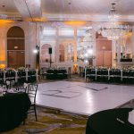Elegant ballroom reception setup with crystal chandeliers, black linens, white centerpieces, and custom dance floor