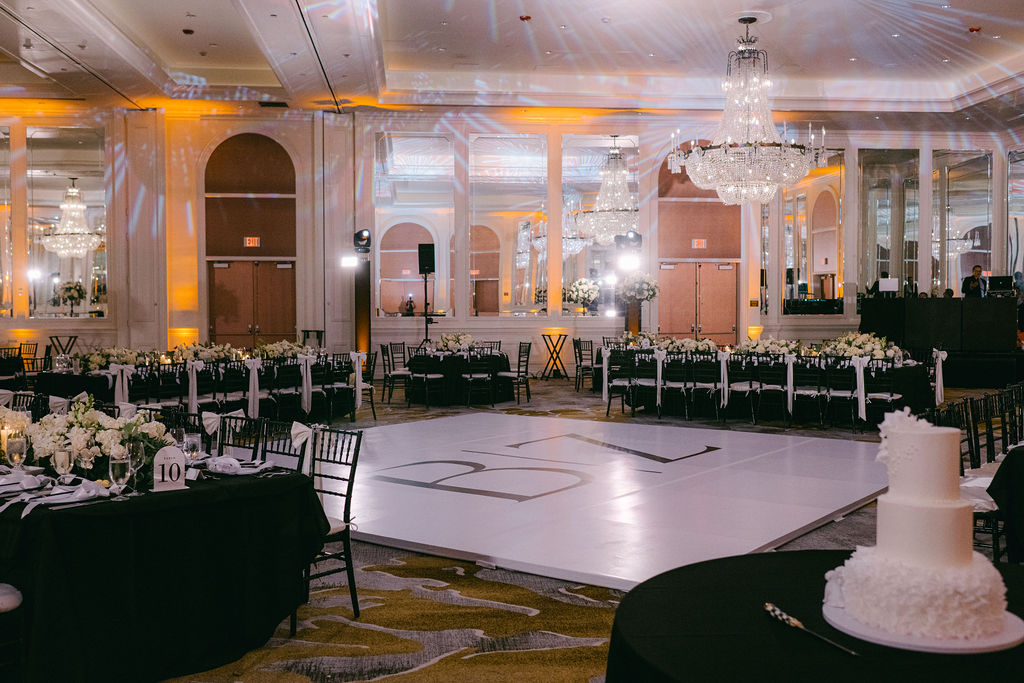 Elegant ballroom reception setup with crystal chandeliers, black linens, white centerpieces, and custom dance floor