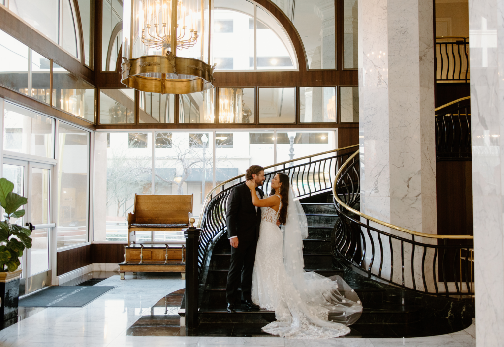 Bride and groom embrace on grand staircase in elegant El Paso hotel lobby