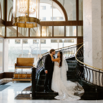 Bride and groom embrace on grand staircase in elegant El Paso hotel lobby