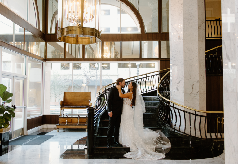 Bride and groom embrace on grand staircase in elegant El Paso hotel lobby