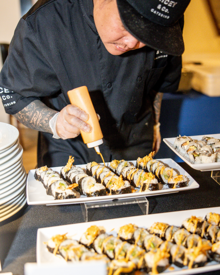 Chef drizzling sauce over artfully arranged sushi platters at wedding reception
