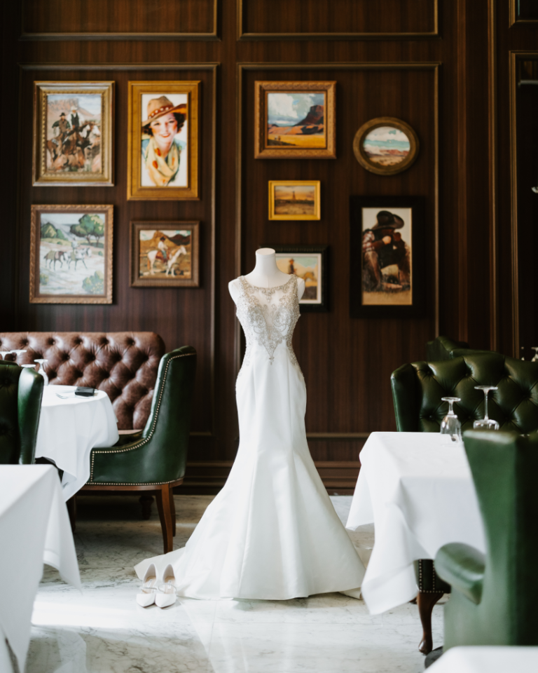 White wedding gown displayed against gallery wall with western artwork and brown leather seating
