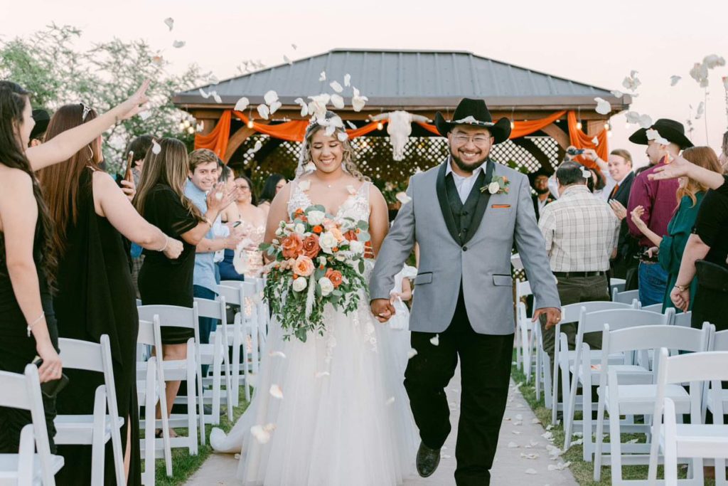 Newlyweds walk down aisle at outdoor El Paso wedding venue as guests toss flower petals