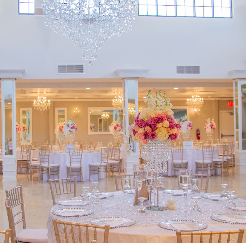 Elegant white ballroom with gold chiavari chairs, crystal centerpieces with pink and coral roses, and ornate chandelier at Grand Gala Events