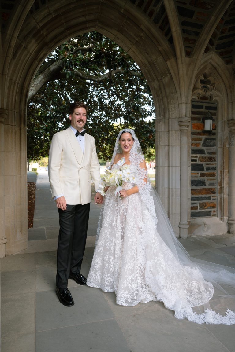 Bride and groom in formal wedding attire standing under stone archway