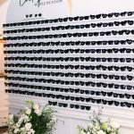 Wedding sunglasses display wall with personalized black sunglasses, white floral arrangements, and disco balls at base