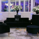 Black lounge furniture with white floral arrangements and personalized signage