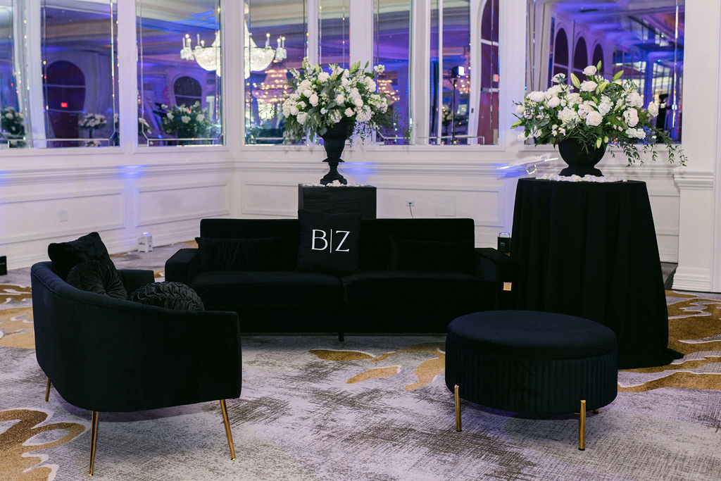 Black lounge furniture with white floral arrangements and personalized signage