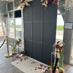 Elegant photo booth backdrop with dark panels, floral arrangements, gold stands, and rose petals for El Paso events
