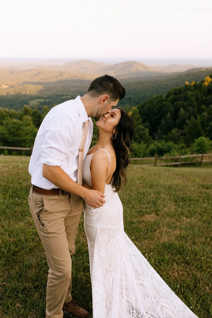 Couple kissing in golden hour light with rolling mountain landscape in background