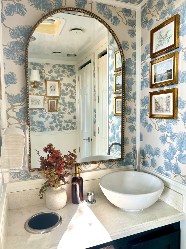 Powder room with blue floral wallpaper, arched mirror, and vessel sink