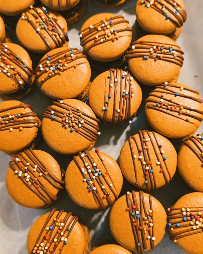 Orange French macarons drizzled with chocolate stripes and colorful sprinkles arranged on a baking sheet