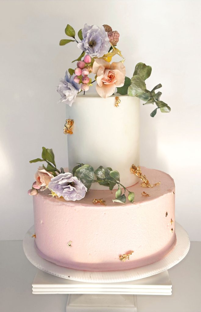 Two-tier wedding cake with blush pink and ivory fondant, decorated with sugar flowers and gold leaf