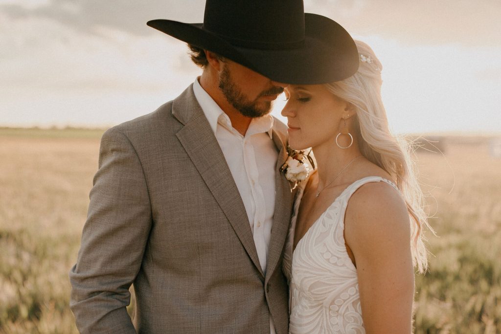 Bride and groom in an intimate moment at golden hour, groom wearing cowboy hat and grey suit, bride in lace wedding dress