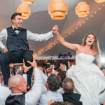 joyful bride and groom during wedding reception being held up by their guests on chairs