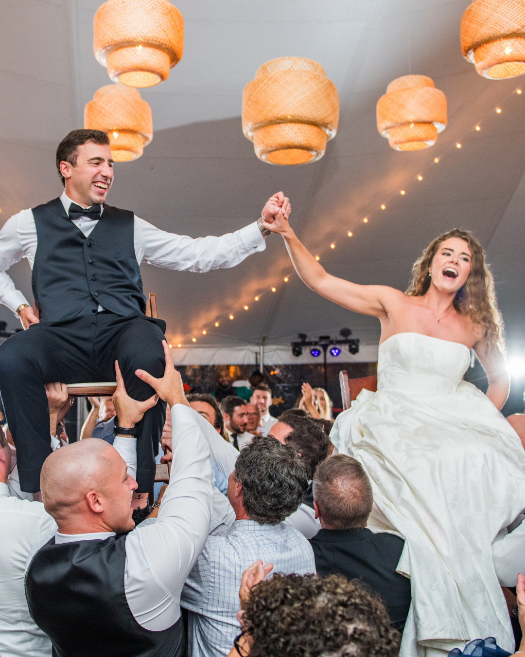 joyful bride and groom during wedding reception being held up by their guests on chairs