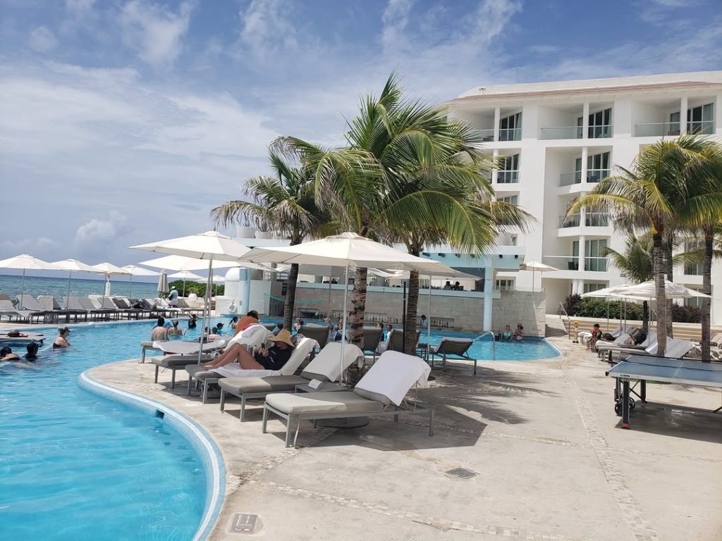Resort poolside with palm trees, white umbrellas, and modern white hotel building