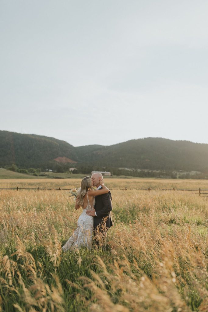 Bride and groom embracing in golden Colorado field with forested mountains in the background