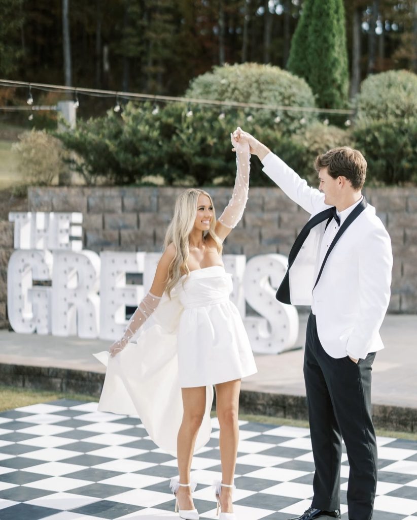 Couple dancing on checkered floor in front of illuminated marquee letters at outdoor garden reception
