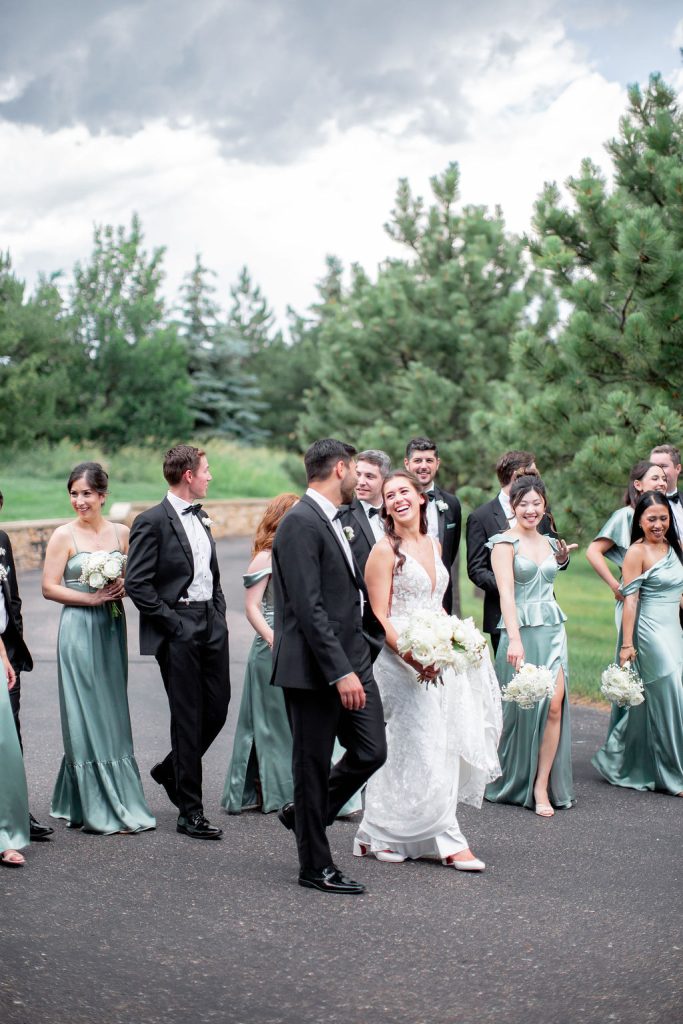 Wedding party walks outdoors with bride and groom at Colorado venue surrounded by evergreen trees
