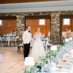 Bride and groom walk through rustic reception venue with stone archways and elegant table settings