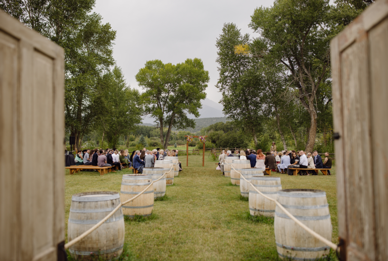Outdoor wedding ceremony framed by vintage doors with wine barrel aisle markers and mountain backdrop