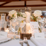 Elegant white wedding reception centerpiece with roses, orchids, candles, and gold table number seven