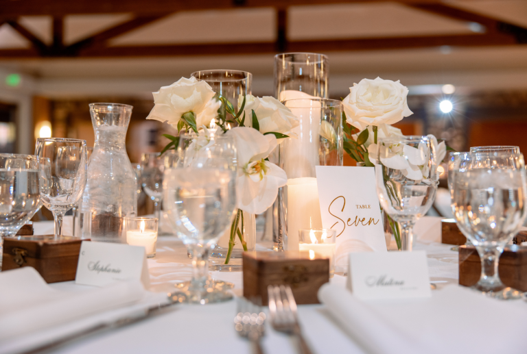 Elegant white wedding reception centerpiece with roses, orchids, candles, and gold table number seven