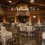 Rustic barn wedding reception with round tables, cross-back chairs, string lights, and candlelit centerpieces