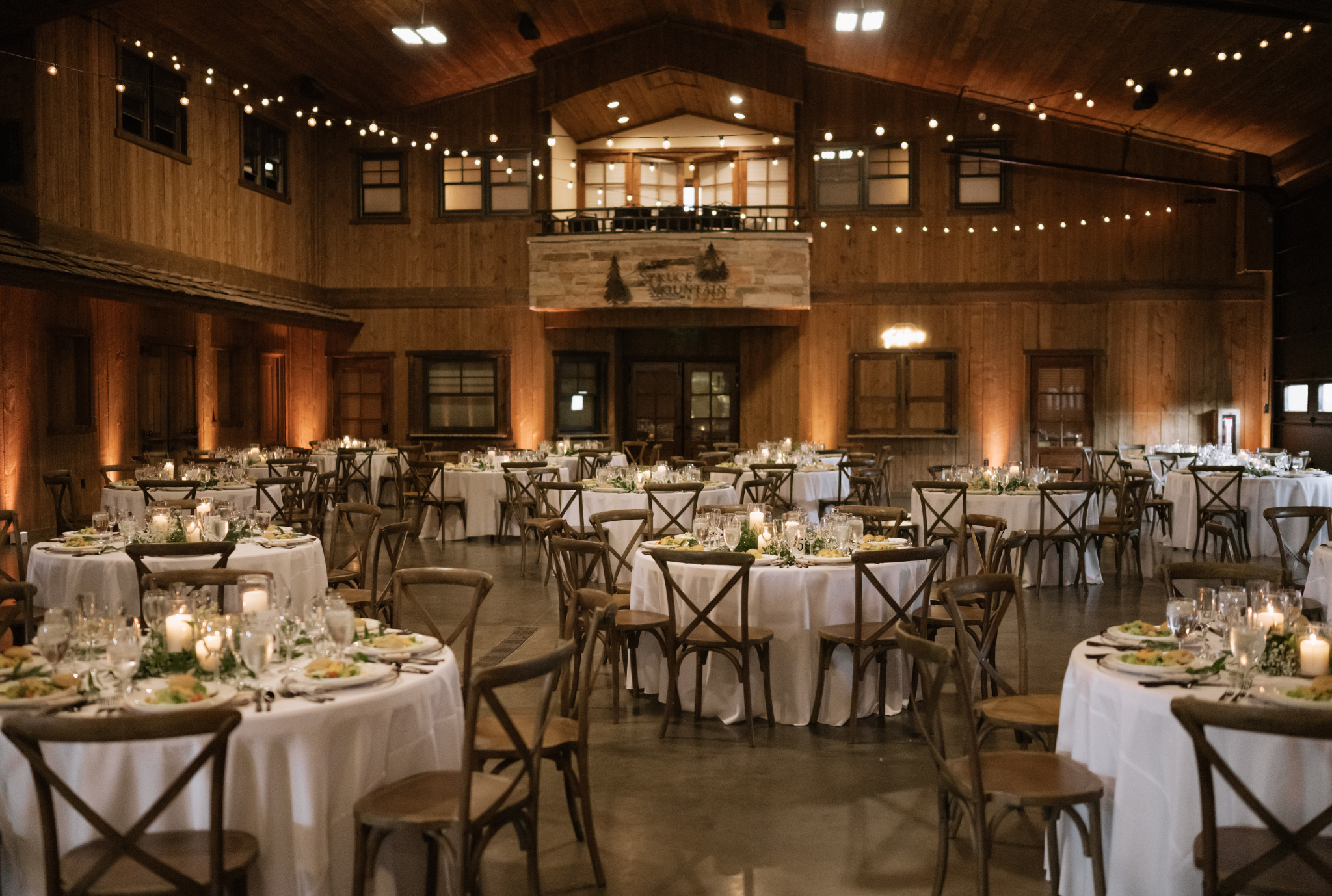 Rustic barn wedding reception with round tables, cross-back chairs, string lights, and candlelit centerpieces