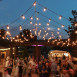 Outdoor wedding reception at dusk with string lights canopy and guests dancing on patio
