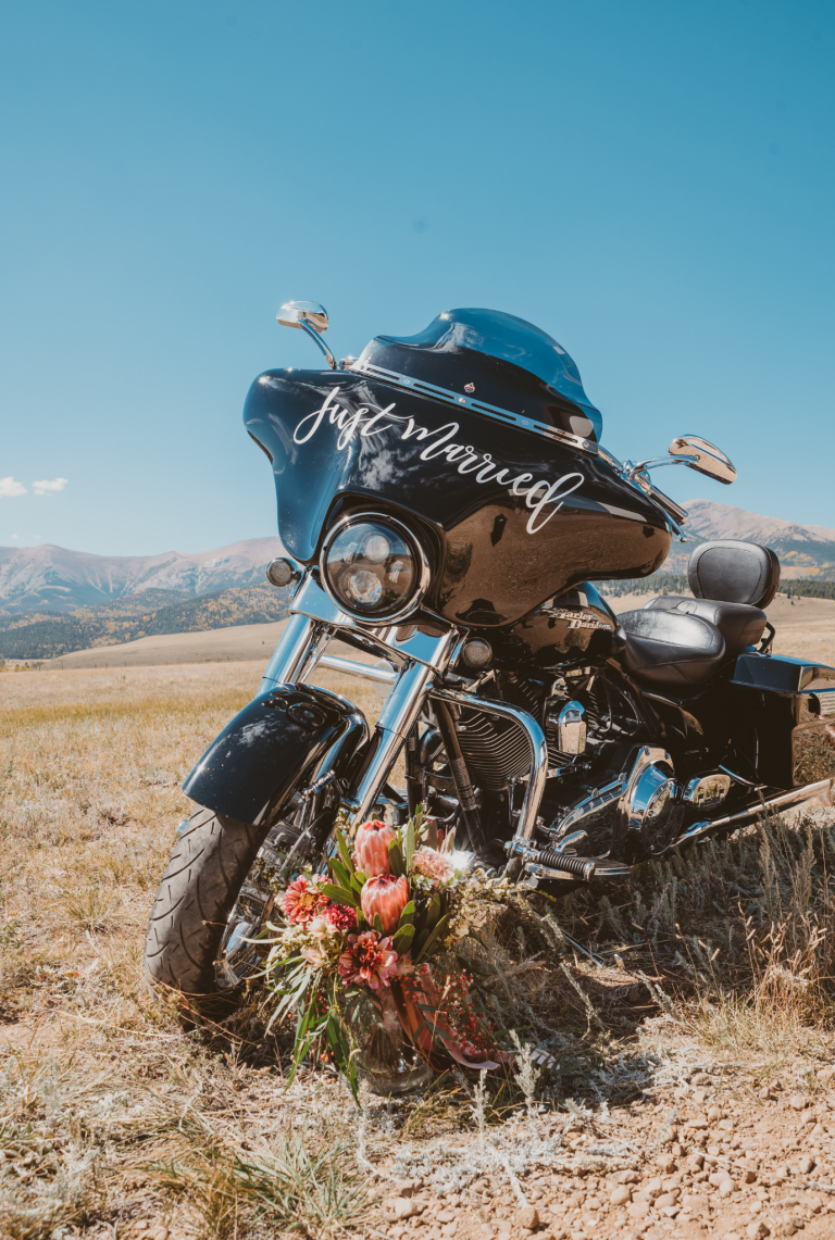 Motorcycle with "just married" sign and floral bouquet in Colorado mountain landscape