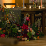 Vibrant floral arrangement with pink, purple, and orange blooms displayed against rustic wooden shelving
