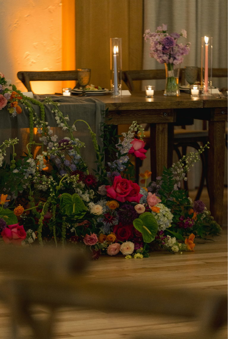 Vibrant floral arrangement with pink, purple, and orange blooms displayed against rustic wooden shelving