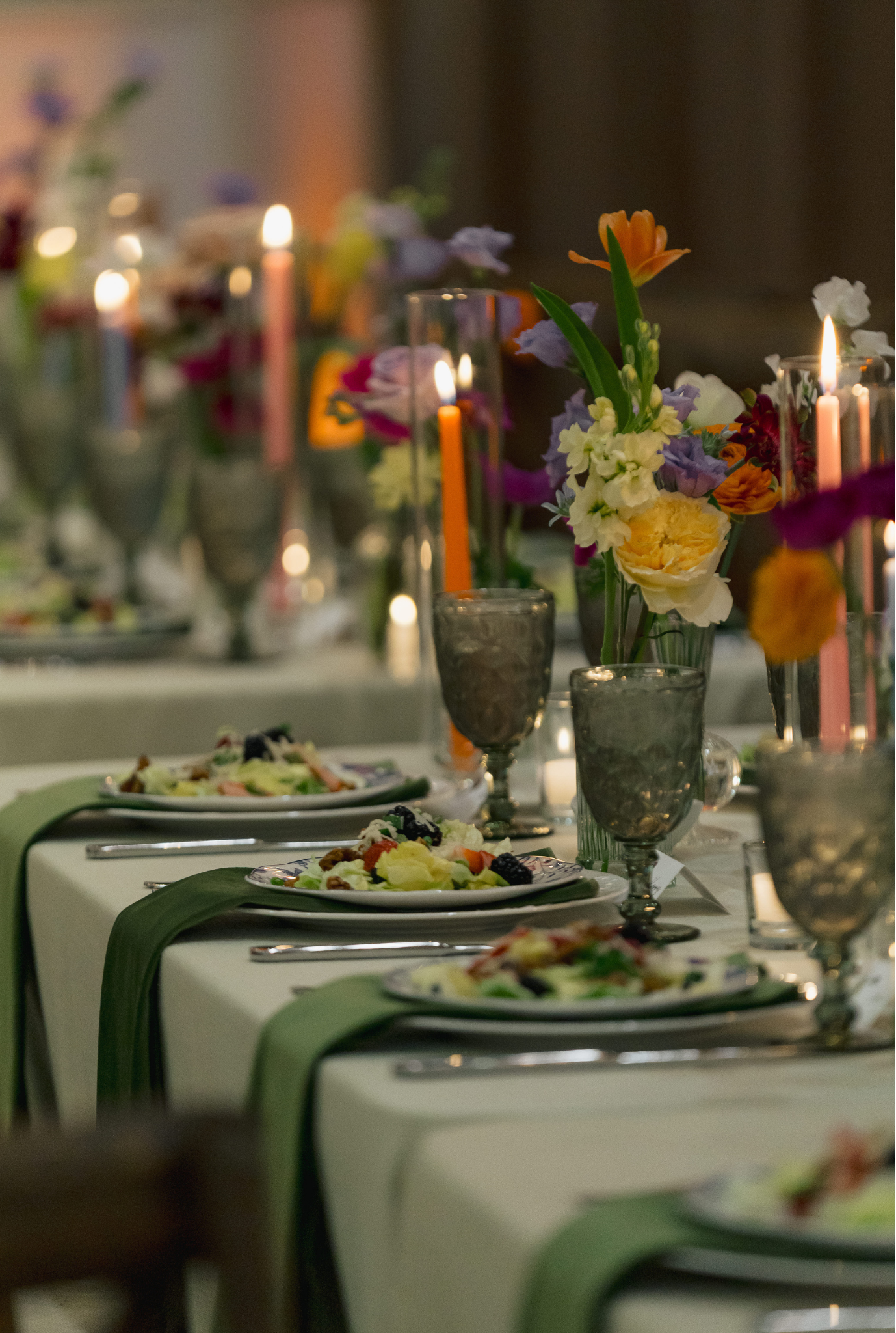 Elegant wedding tablescape with colorful floral centerpieces, candles, and green table runner