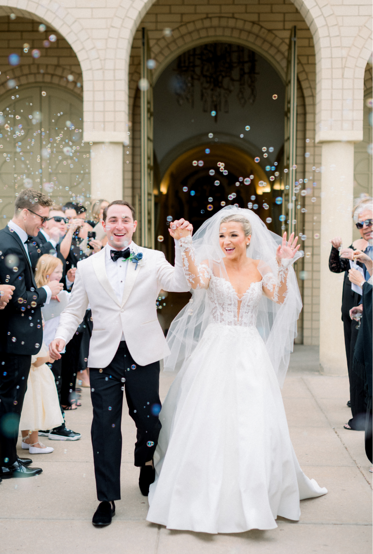 Newlyweds exit church through bubble send-off line outside stone arched entrance