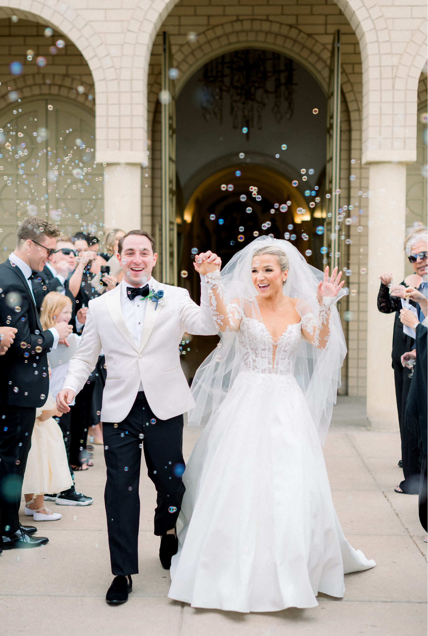 Newlyweds exit church through bubble send-off line outside stone arched entrance