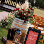 Outdoor wedding reception table with burgundy and greenery floral arrangement and welcome signage