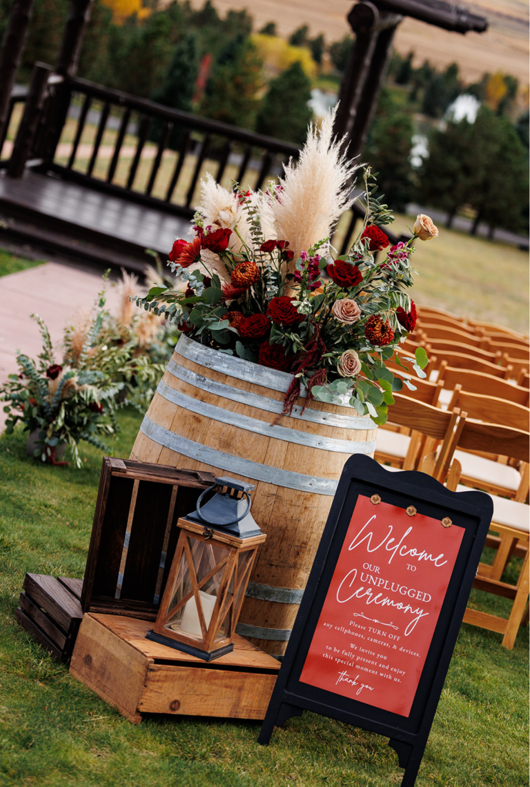 Outdoor wedding reception table with burgundy and greenery floral arrangement and welcome signage