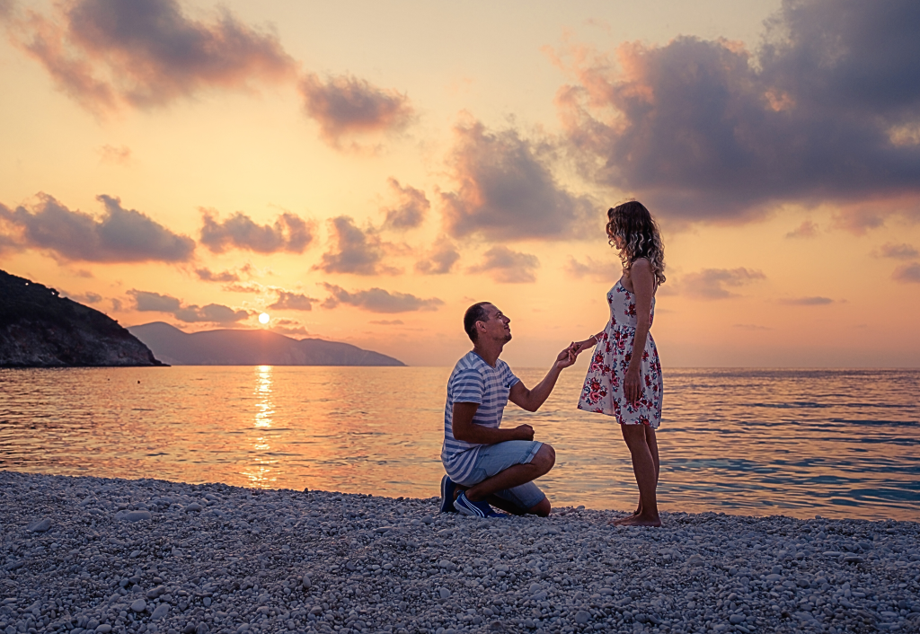 Man proposing on one knee to woman at beach during golden hour sunset
