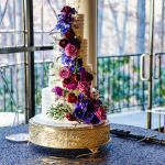 three tiered wedding cake with bold and colorful florals, in dark blue, pink and purple