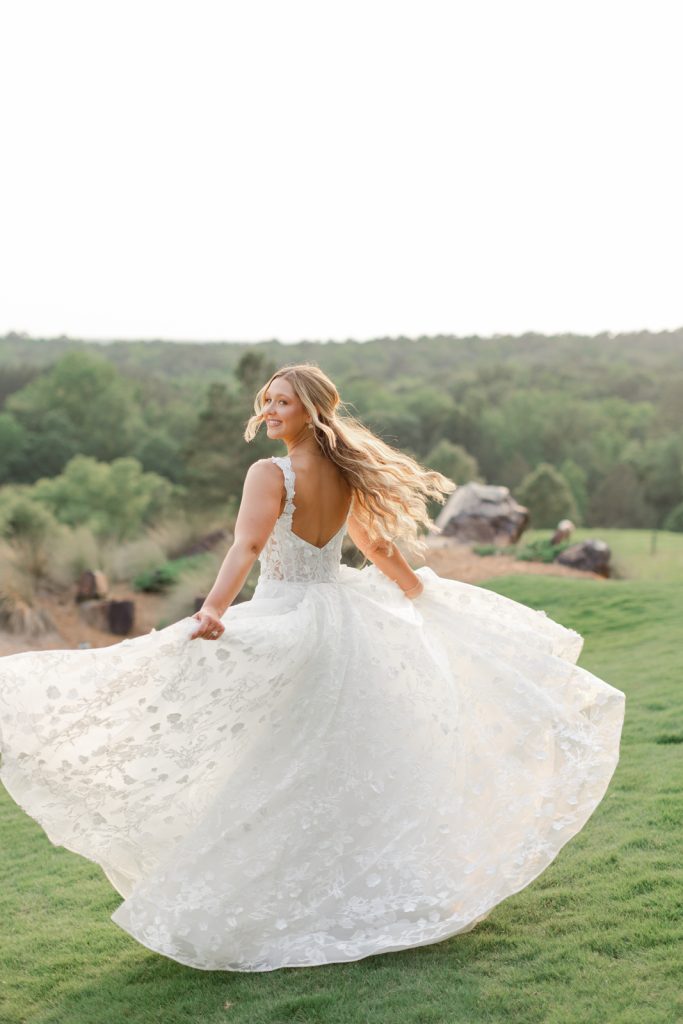 Bride twirling in lace wedding gown at golden hour on landscaped lawn overlooking rolling hills
